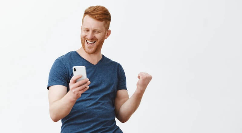 Homem branco comemorando enquanto olha para a tela de um celular.